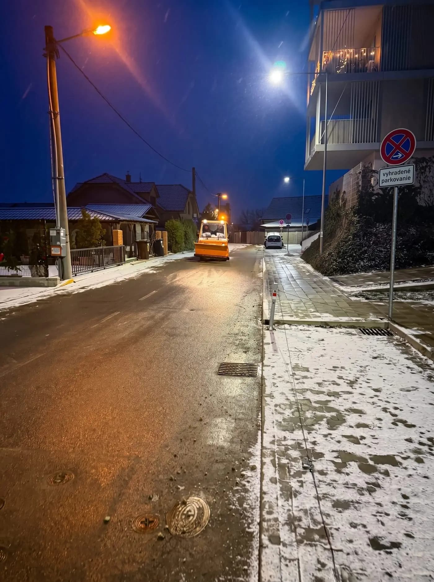 Zasnežená ulica v obytnej zóne počas nočnej zimnej údržby