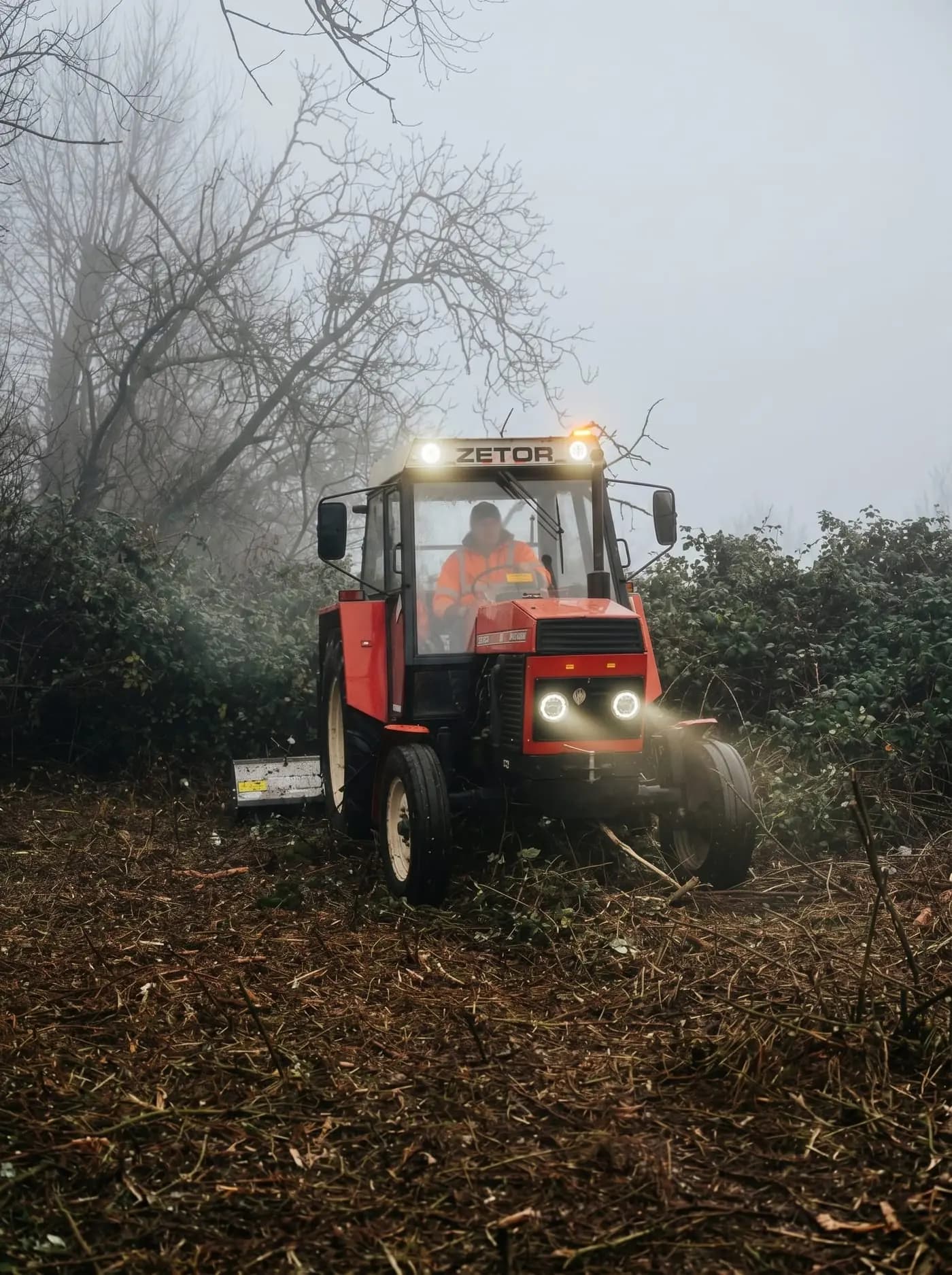 Traktor Zetor s mulčovačom pri čistení zarasteného terénu v hmle